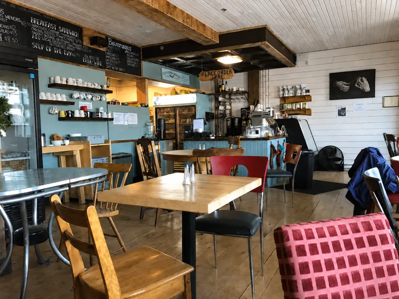 Wooden tables and chairs facing the blue coffee counter inside Cottage Cafe.